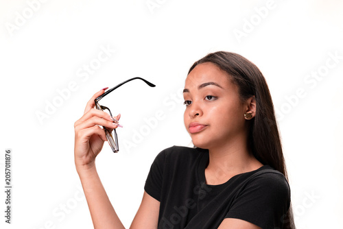 Skeptical young latina woman holding eyeglasses and looking away isolated on white background.