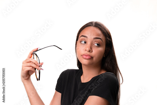 Suspicious young latina woman holding eyeglasses and looking aside isolated on white background.