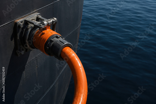 New orange fuel hose connected to ship hull against blue ocean background, showcasing maritime industry and transportation