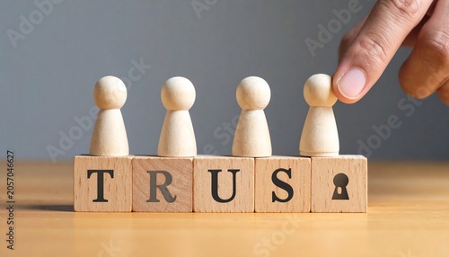 Four wooden figurines standing in row behind blocks spelling TRUST on wooden surface, plain softly lit background, symbolic representation of teamwork, relationships, communication, unity, reliability