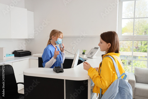 Medical receptionist in face mask on phone assisting patient with payment at ...