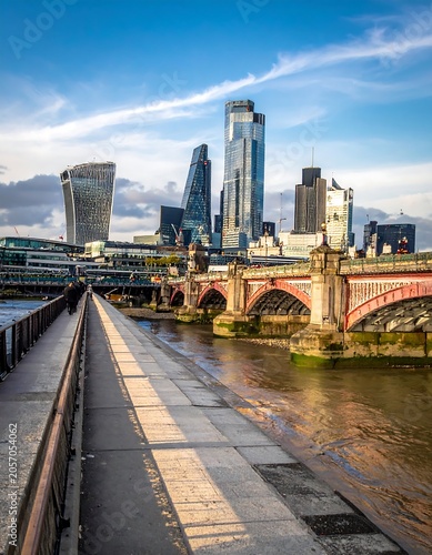 A cityscape with a river and bridge under a blue sky with white clouds