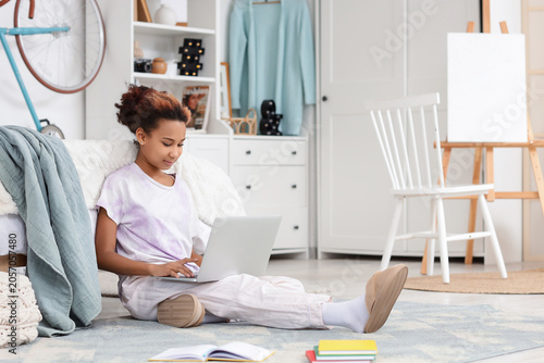 Teenage African-American girl studying with laptop in bedroom