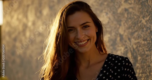 Smiling woman with long hair in a polka dot dress, sunset glow, serene outdoor setting