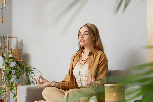 Beautiful young woman meditating on sofa at home. Zen concept