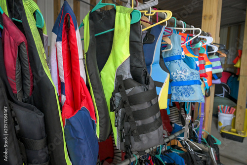 Billede på lærred Collection of colorful life jackets hanging on a storage rack inside a boathouse or recreational facility