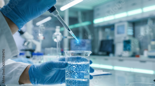 Researcher using pipette dropping liquid into chemical beaker in science lab.