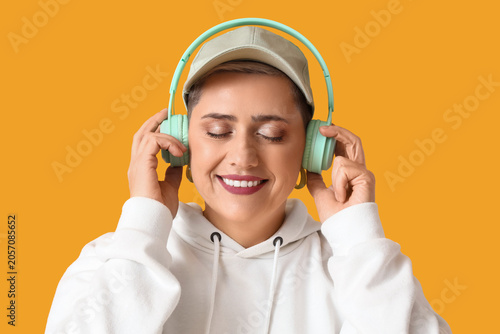 Happy mature blonde woman with short hair in headphones on yellow background