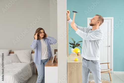 Fényképezés Young woman suffering from noisy neighbour hammering nail at home