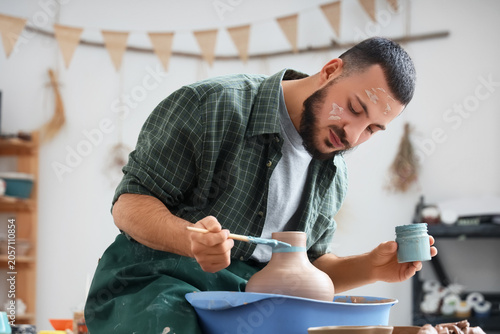 Young male potter painting ...