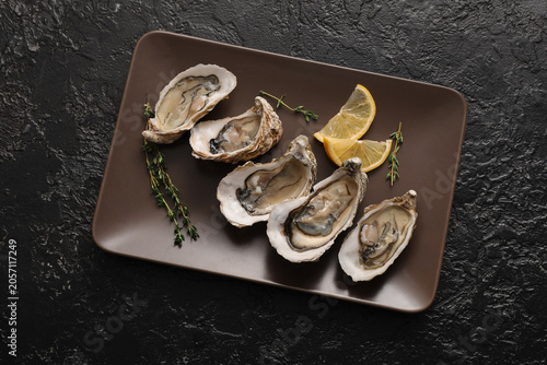 Photography Fresh raw oysters with lemon slices and thyme on a brown plate, gourmet seafood
