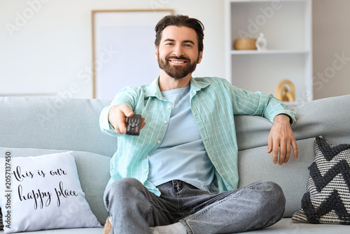 Young man with remote controller watching TV on sofa at home