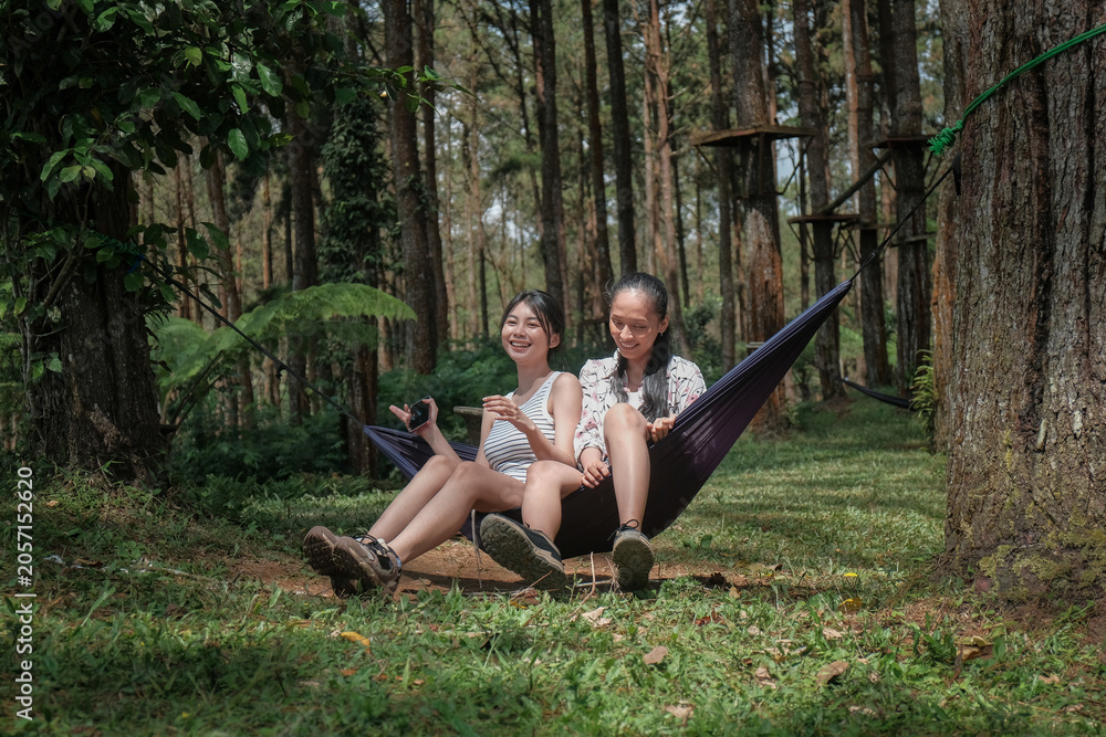 Obraz premium Asian Indonesian Female Friends Relaxing in Hammock During Forest Camping Trip