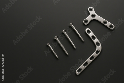 Orthopedic surgical steel bone plate and screw implant set arranged on dark matte surface, medical hardware for bone fixation surgery