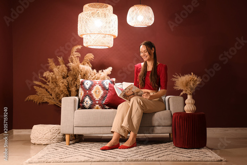 Photos Smiling woman reading magazine on sofa in cozy living room with bohemian decor a