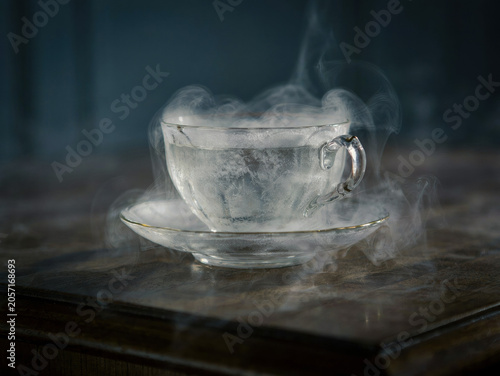 Transparent teacup made of ice with thick smoke or steam rising from the liquid on a dark wooden table. Generative AI.