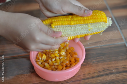 A person is cutting a corn on a table. The corn is in a bowl and the person is using a knife to cut it