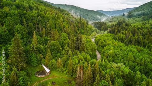 Tableau sur toile Mountain forest valley with a riverside shelter and footpaths seen by drone as t