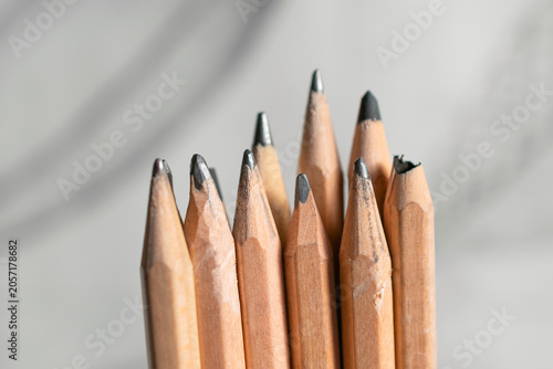 Several drawing pencil tips in various stages of sharpness stand in front of a blurry background with some curved lines on it.