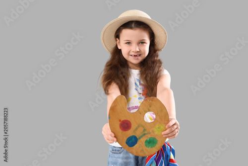 Smiling little girl in straw hat holding artists palette with colorful paints...