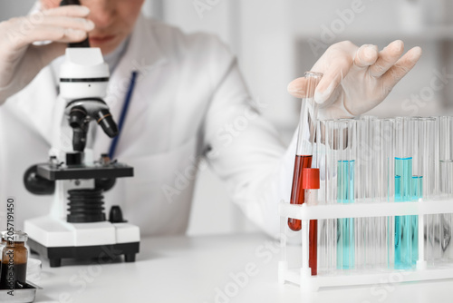 Female scientist with test tube looking through microscope in laboratory, clo...