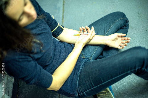 Person sitting on the floor  preparing to inject with a syringe.