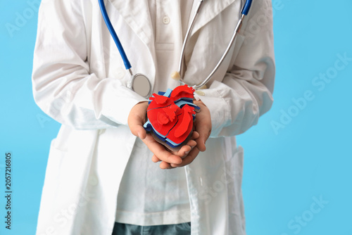 Little doctor with paper heart on blue background, closeup