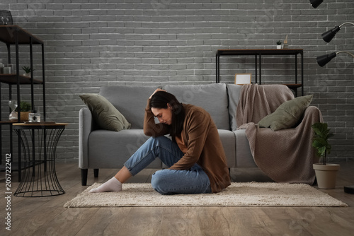 Depressed young woman sitting on carpet at home
