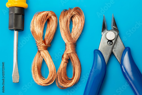 Copper wire coils with screwdriver and wire cutter on blue background. Electrician tools and copper wire components for electricity repair job.