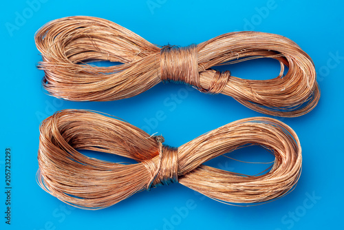 Copper wire coils on a blue background. Industrial raw material for electrical cables, electronics manufacturing and recycling concepts. Two bundles of bright copper wires. Closeup of metal wire.