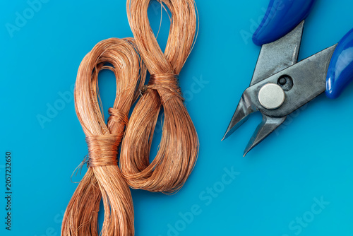 Copper wire coils with side cutters on blue background. Professional electrical tools, components, recycling raw materials and industrial equipment concept.