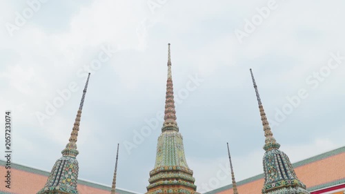 Tilt Up camera movement of ornate Buddhist chedis and spires at Wat Pho temple showcase intricate traditional Thai architecture and colorful tile mosaic details under a clear sky in Bangkok, Thailand