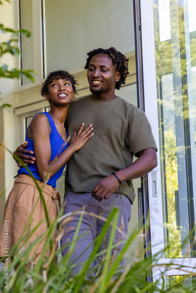 Obraz premium African American couple standing in doorway, leaning together near sliding glass door with plants