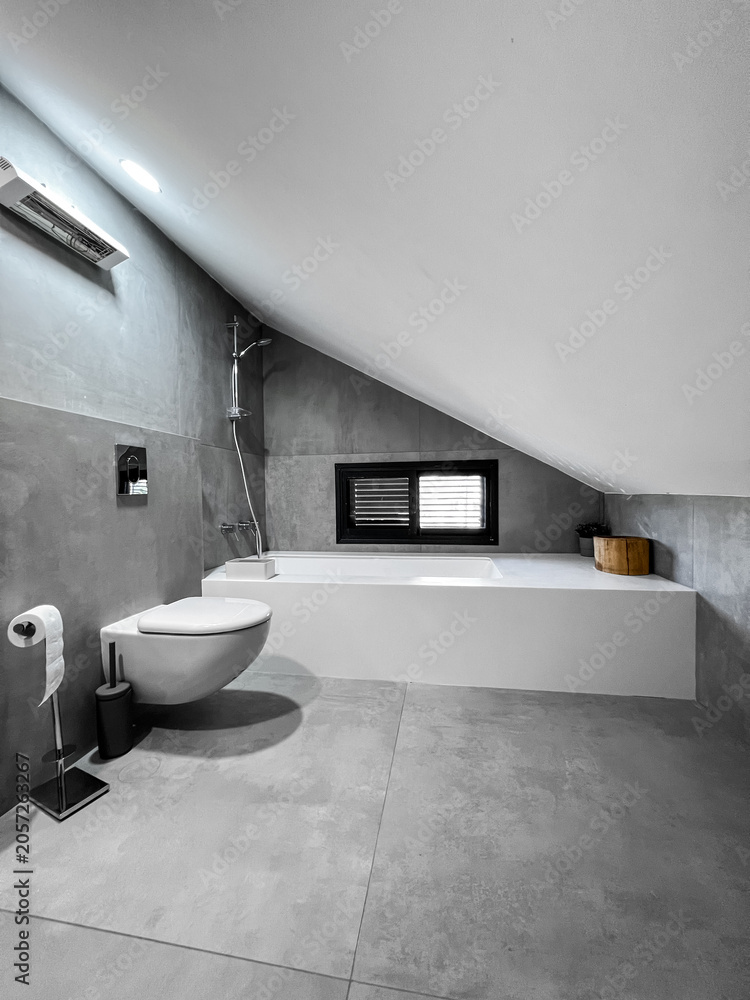 Fototapeta premium Modern minimalist bathroom interior design with gray concrete walls, white bathtub, and wall-mounted toilet