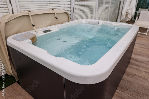 Schilderij op canvas Outdoor hot tub with bubbling water and beige cover on a wooden deck for relaxat