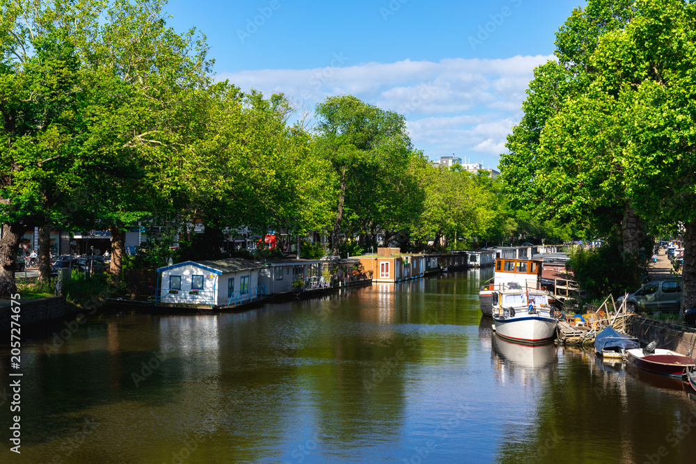 Fototapeta premium Tree-lined canal with houseboats and boats in Amsterdam, Netherlands
