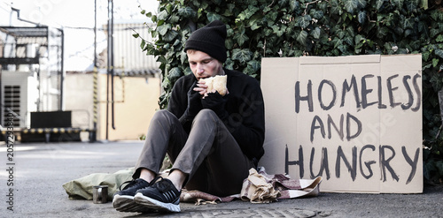 Cuadro en lienzo Homeless man with cardboard eating bread on street