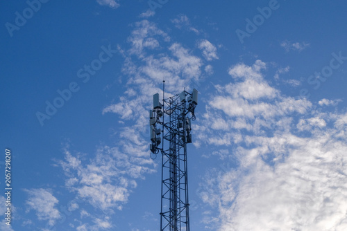 A tall cell phone tower against a blue sky and white clouds.