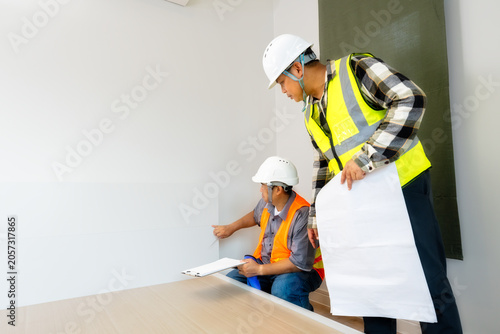 Foto Engineers' Meticulous Detail Check for Room Quality:Engineers precisely inspecting the lower wall and baseboard areas in a new room,ensuring comprehensive quality assurance from top to bottom