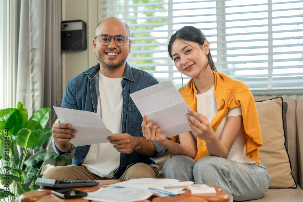 Obraz premium Young couple in the story begin their life together planning their future and managing finances and expenses. Happy Asian husband and wife calculating income and bills to plan for investment.