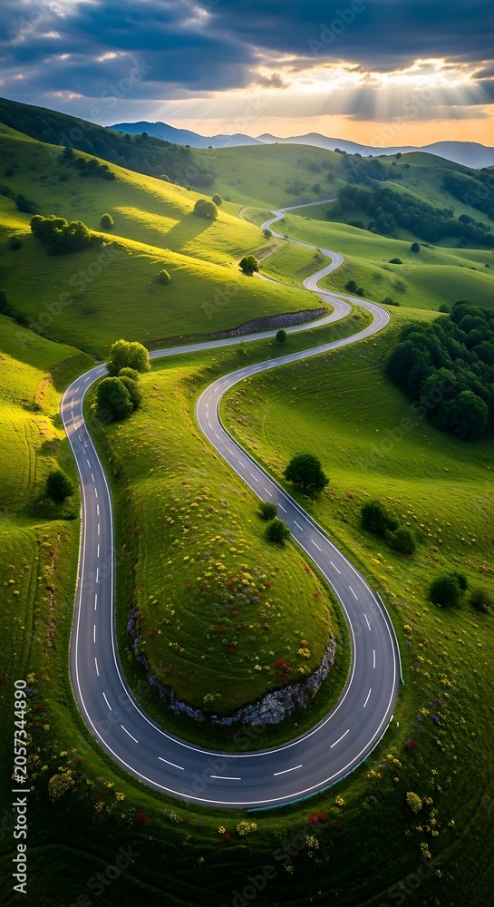 Fototapeta premium Winding road through rolling green hills with dramatic sunlight and shadows