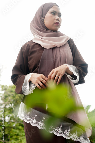 Foto Confident Asian Muslim woman in modest dress looking away behind blurred foreground leaves