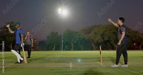 Bowler bowling, indian batsman playing stroke scoring runs on pitch with floodlights, copy space