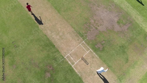 Teenage bowler running, ball at club ground, batsmen sprinting retrieving it to bowl