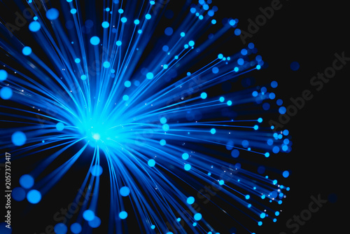 Glowing blue optical fiber strands emit bright light, representing data transmission and digital communication technology.