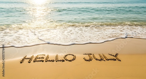 Hello july written in sand on a beach at sunrise