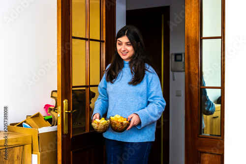 Woman holding bowls of snacks, preparing for special event, hosting friends at home
