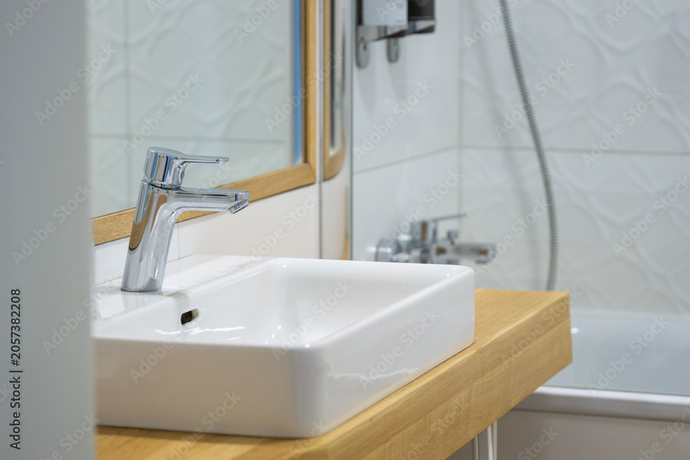 Fototapeta premium modern bathroom sink with a chrome faucet on a light wood countertop in front of a white tiled wall and mirror