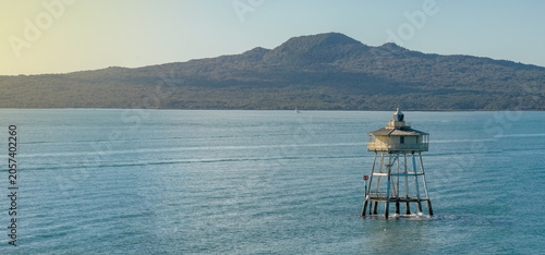 Auckland's Rangitoto Island is visible in the distance from the historic Bean Rock Lighthouse in Waitemata Harbour, New Zealand. The lighthouse guides ships.