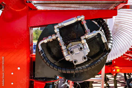 Photos Tight view of a black hose coiled on a metal reel mounted to bright red painted industrial machinery